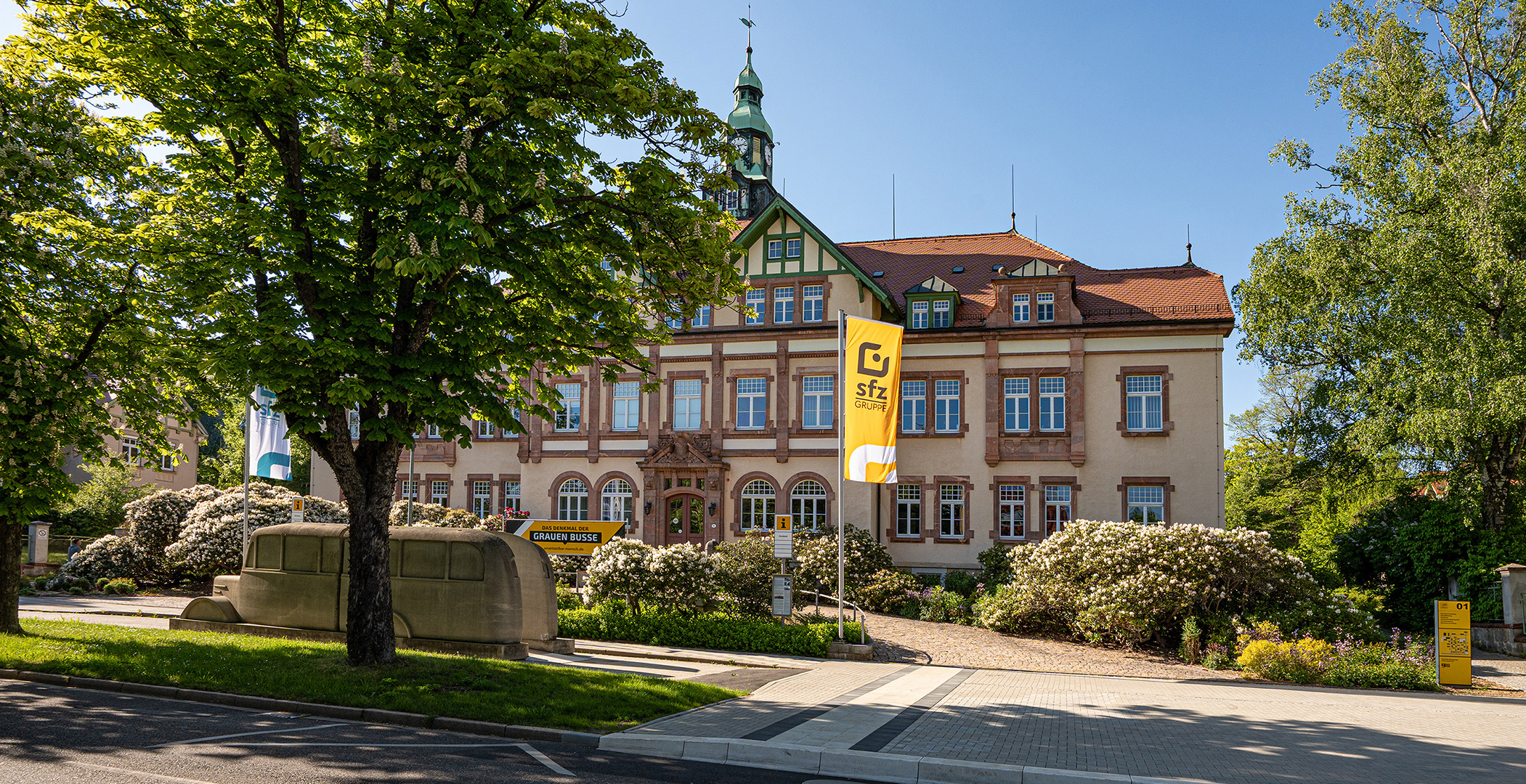 FZ00277_WEB_Website_Cover_S_sRGB Frontansicht alt gebautes Haus mit Flagge sfzGruppe davor.